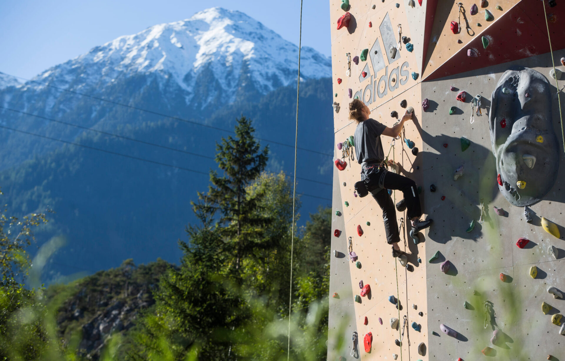 A climber on the outer wall of the climbing tower at AREA 47 in Ötztal, Tyrol, with a mountain panorama in the background