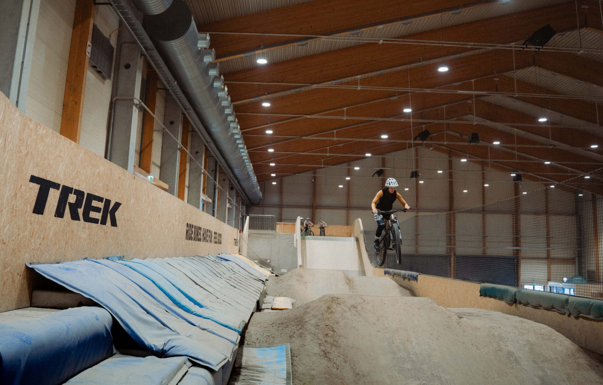 Mountain bikers jumping off a wooden ramp in the AREA 47 indoor bike park in Ötztal, Tyrol