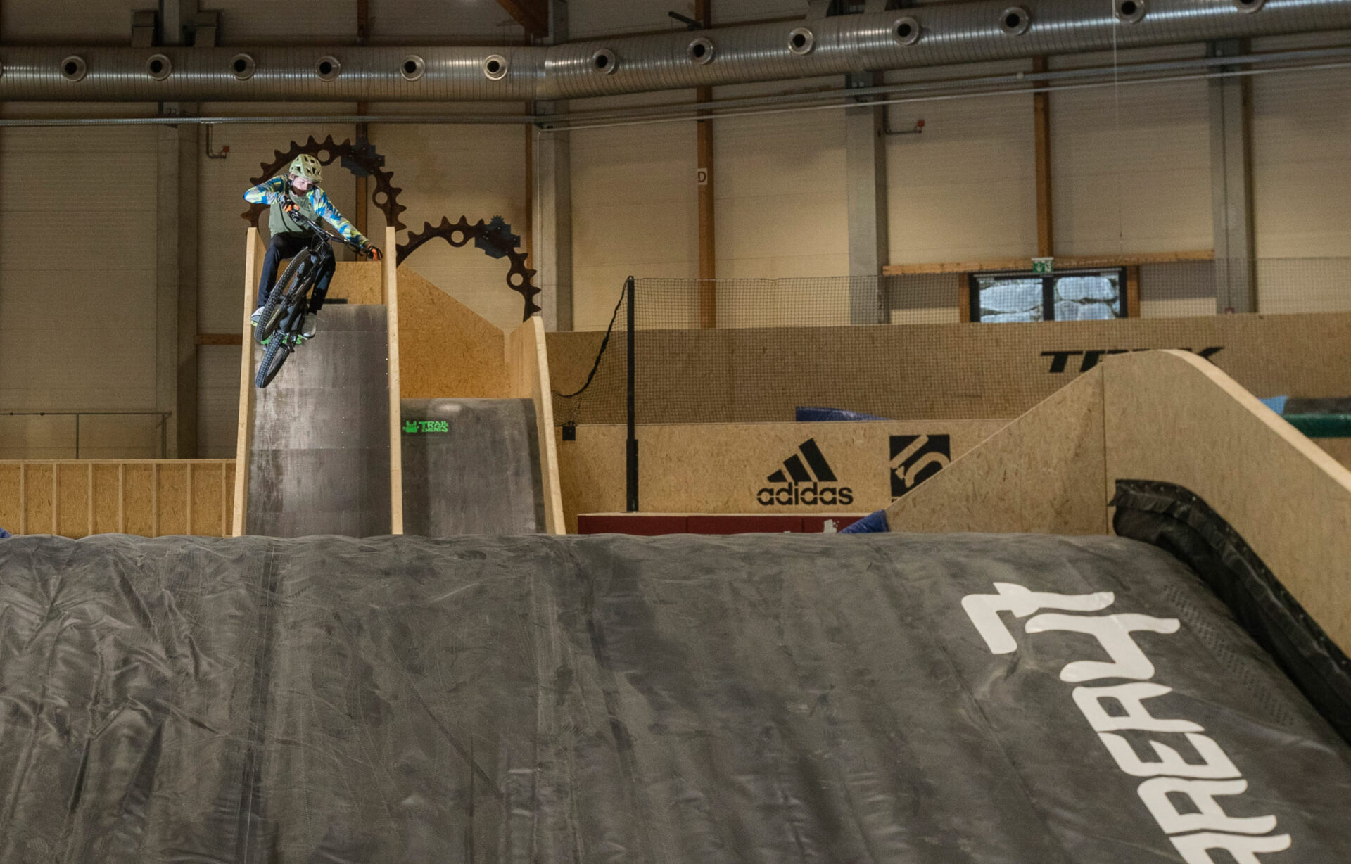 Mountain bikers jumping off a wooden ramp in the AREA 47 indoor bike park in Ötztal, Tyrol