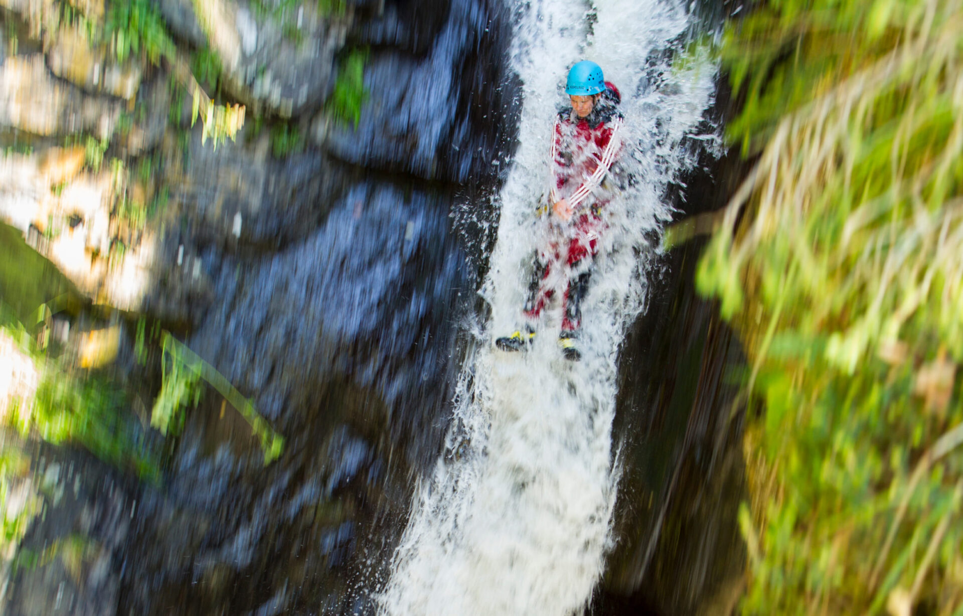 Person in roter Canyoning-Ausrüstung rutscht durch einen Wasserfall in einer Schlucht in der AREA 47 im Ötztal, Tirol.