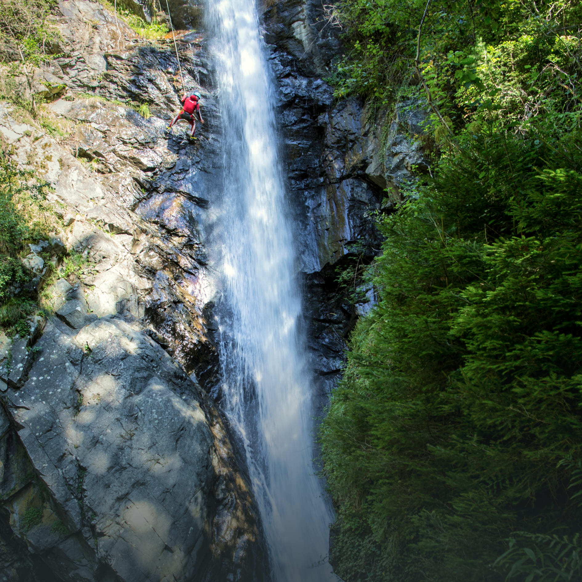 Person beim Abseilen an einem Wasserfall in der AREA 47 im Ötztal, Tirol, umgeben von Felsen und grüner Vegetation