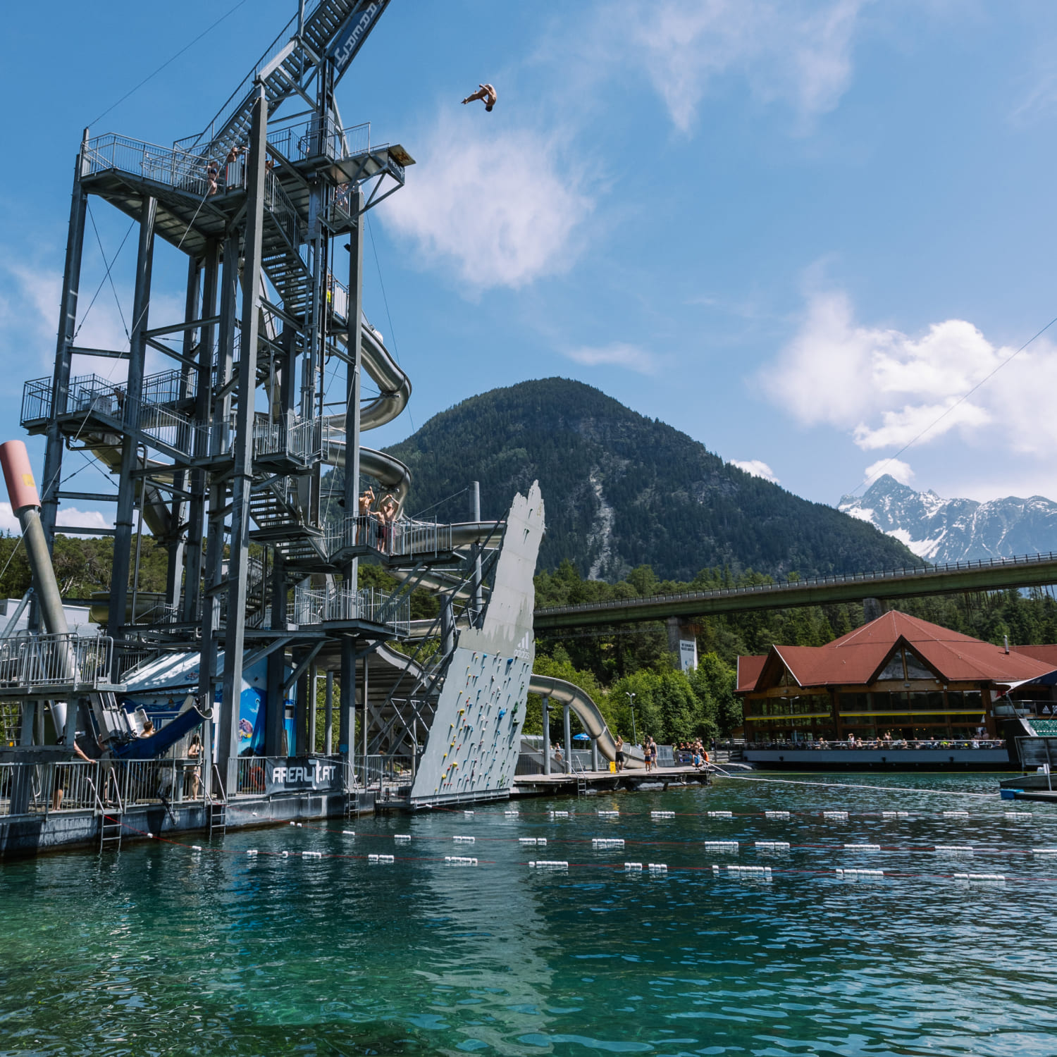 Diving tower in the Water AREA at AREA 47 in Ötztal, Tyrol, with jumper in the air and surrounding mountain landscape