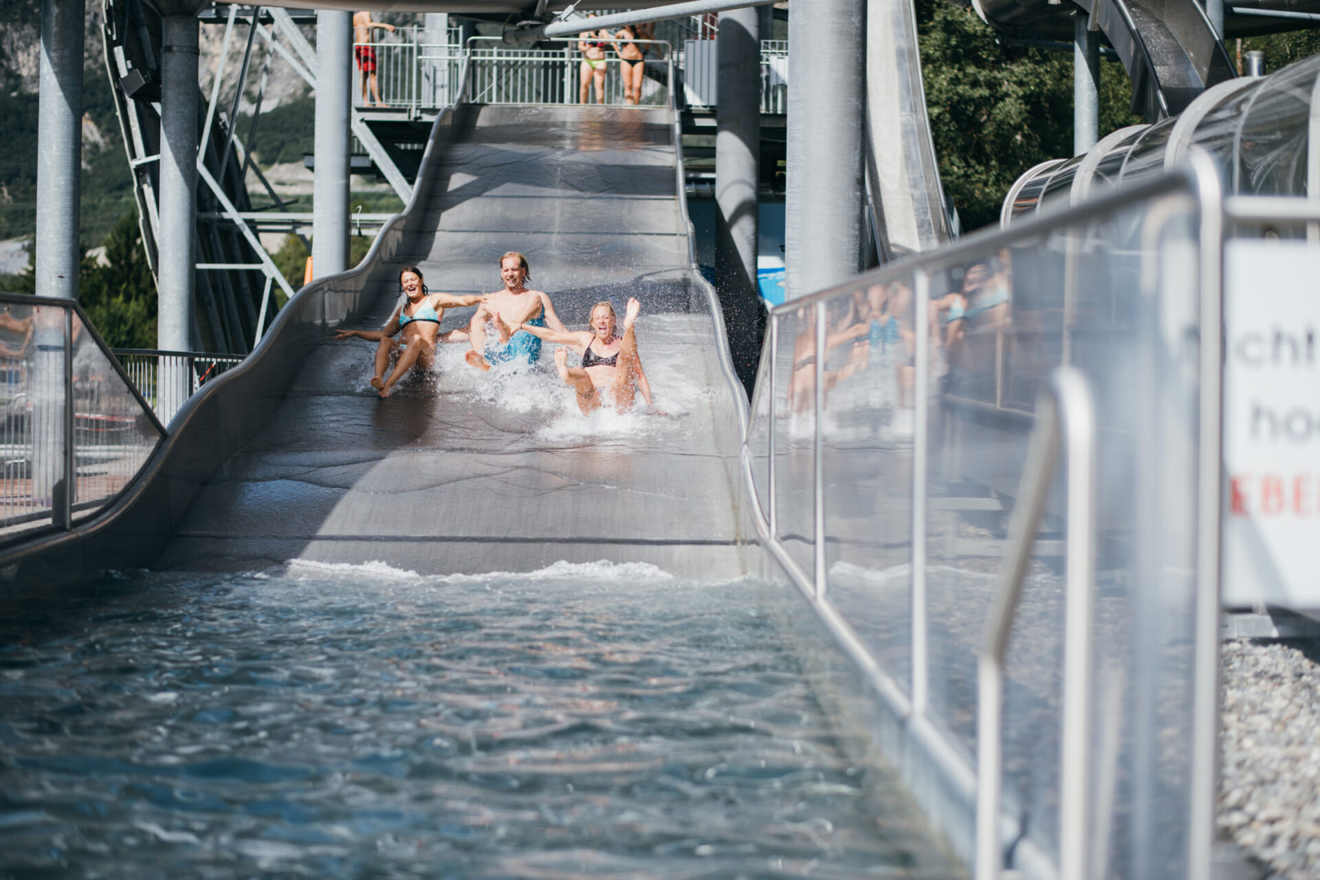 Three people slide down a wide water slide together at AREA 47 in Ötztal, Tyrol