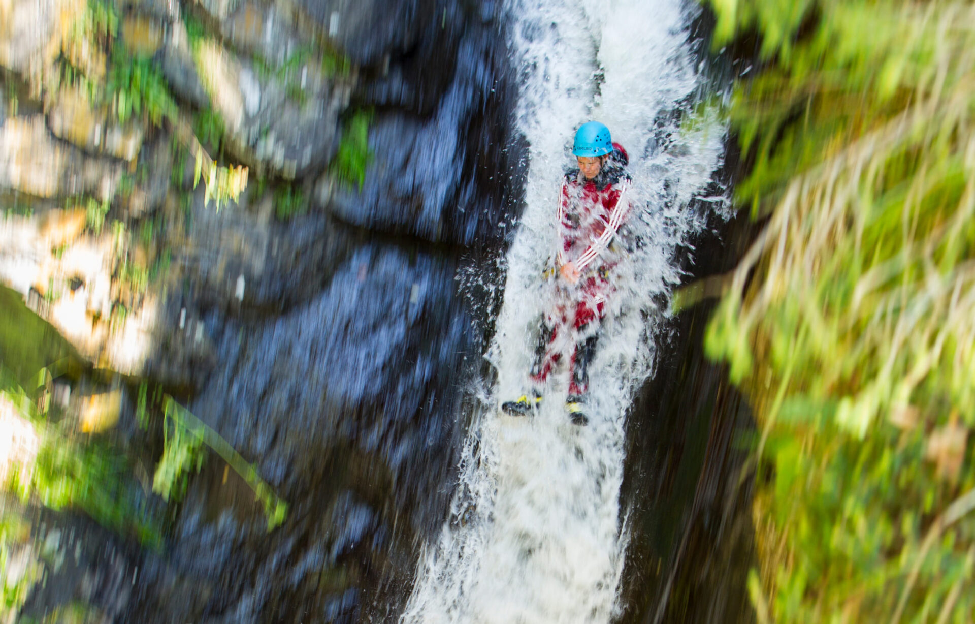 Person in roter Canyoning-Ausrüstung rutscht durch einen Wasserfall in einer Schlucht in der AREA 47 im Ötztal, Tirol.