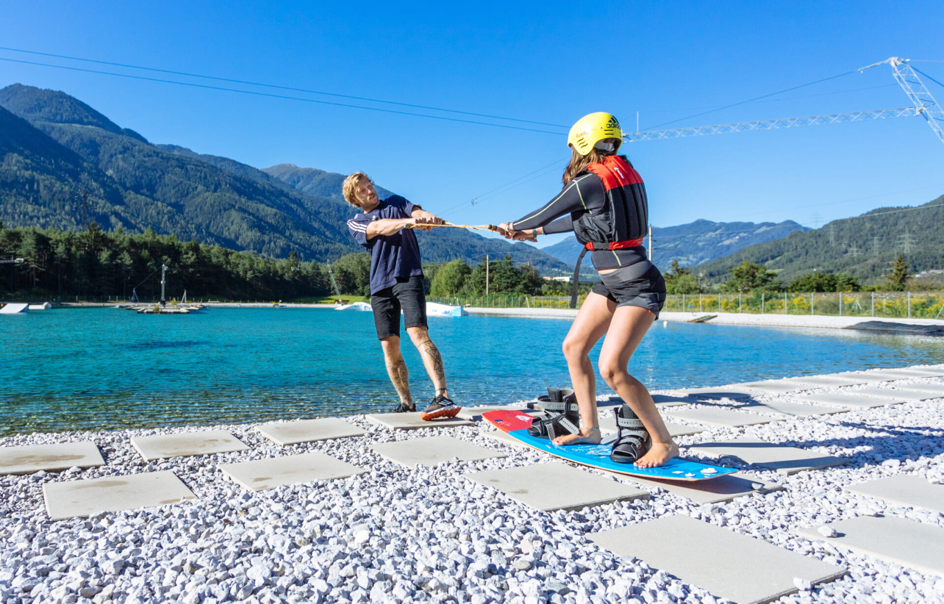 Wakeboard coach assisting a beginner with the handle near the shore at AREA 47 in the Ötztal, Tyrol.