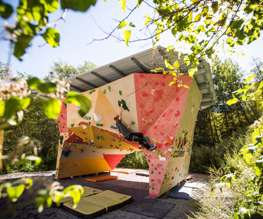 Person bouldert an einer Outdoor-Kletterwand in der AREA 47 im Ötztal, Tirol, umgeben von Matten