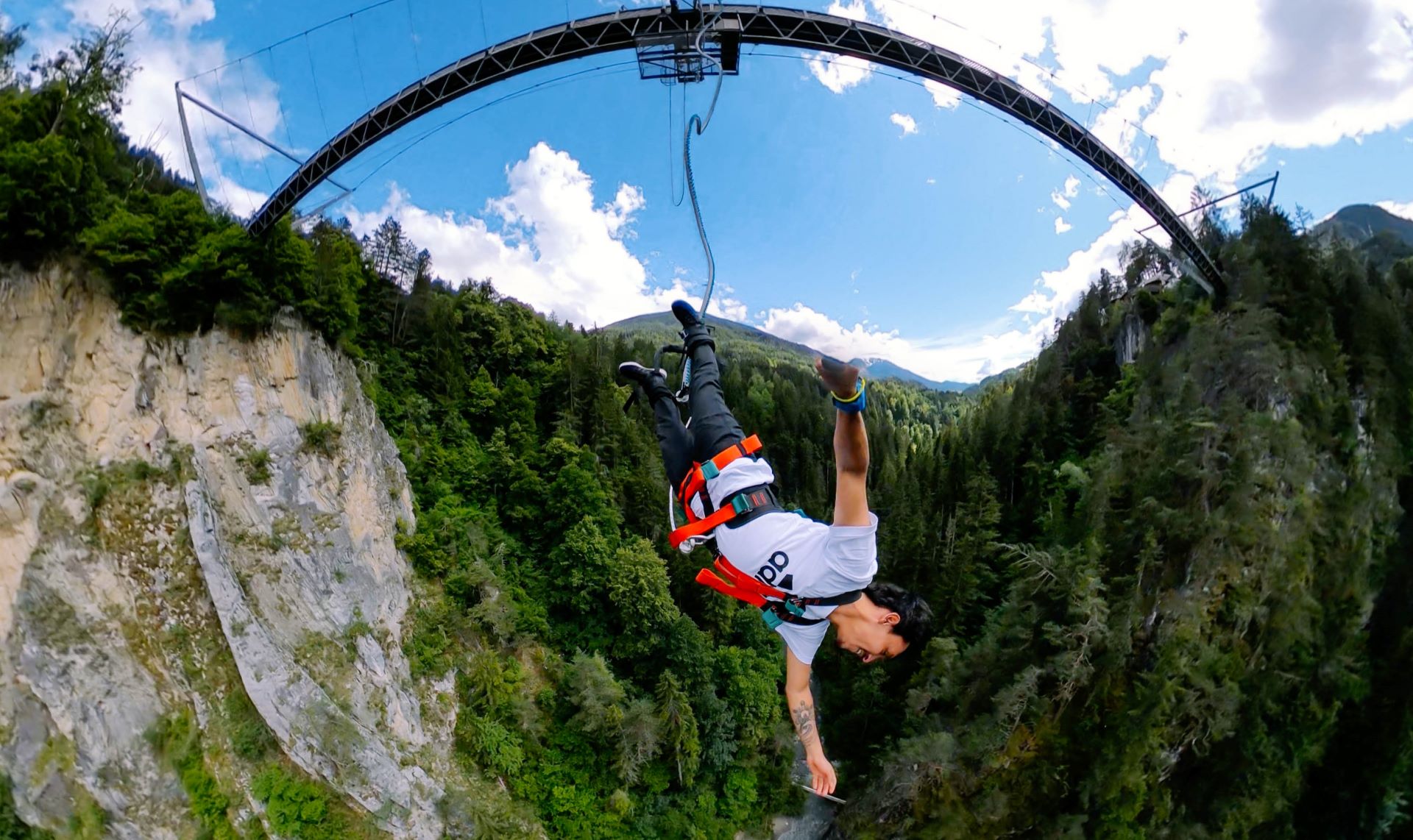 Person bungy jumping from the AREA 47 bridge, surrounded by steep rock faces and forest