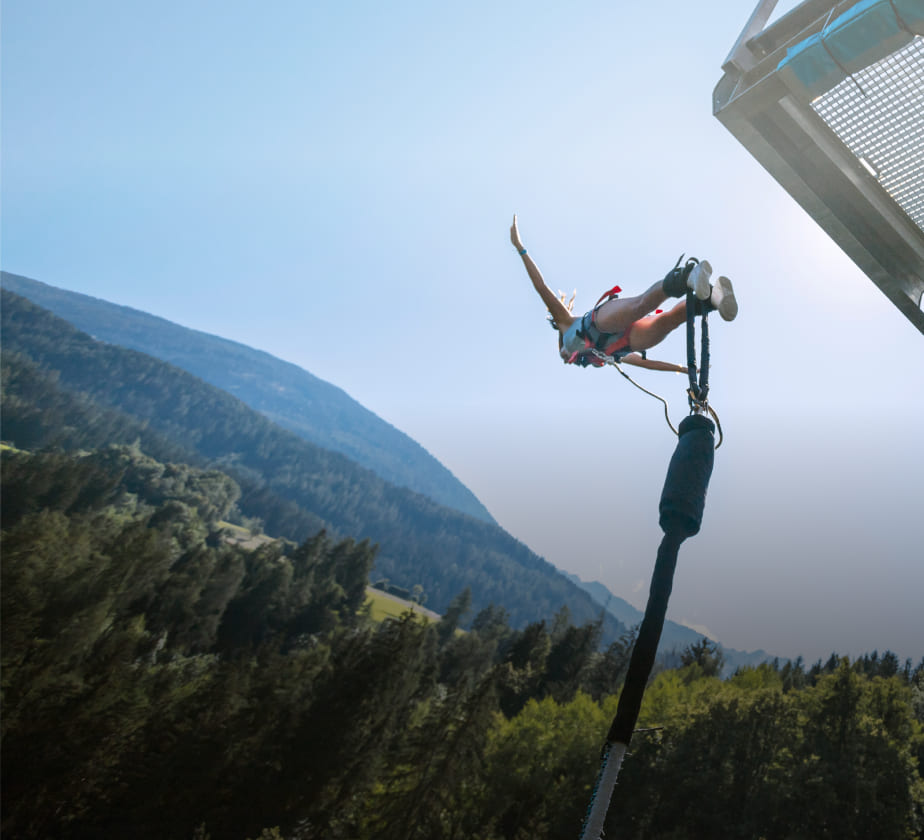 Person beim Bungee-Sprung von einer Plattform in der AREA 47 im Ötztal, Tirol, vor bewaldeter Berglandschaft