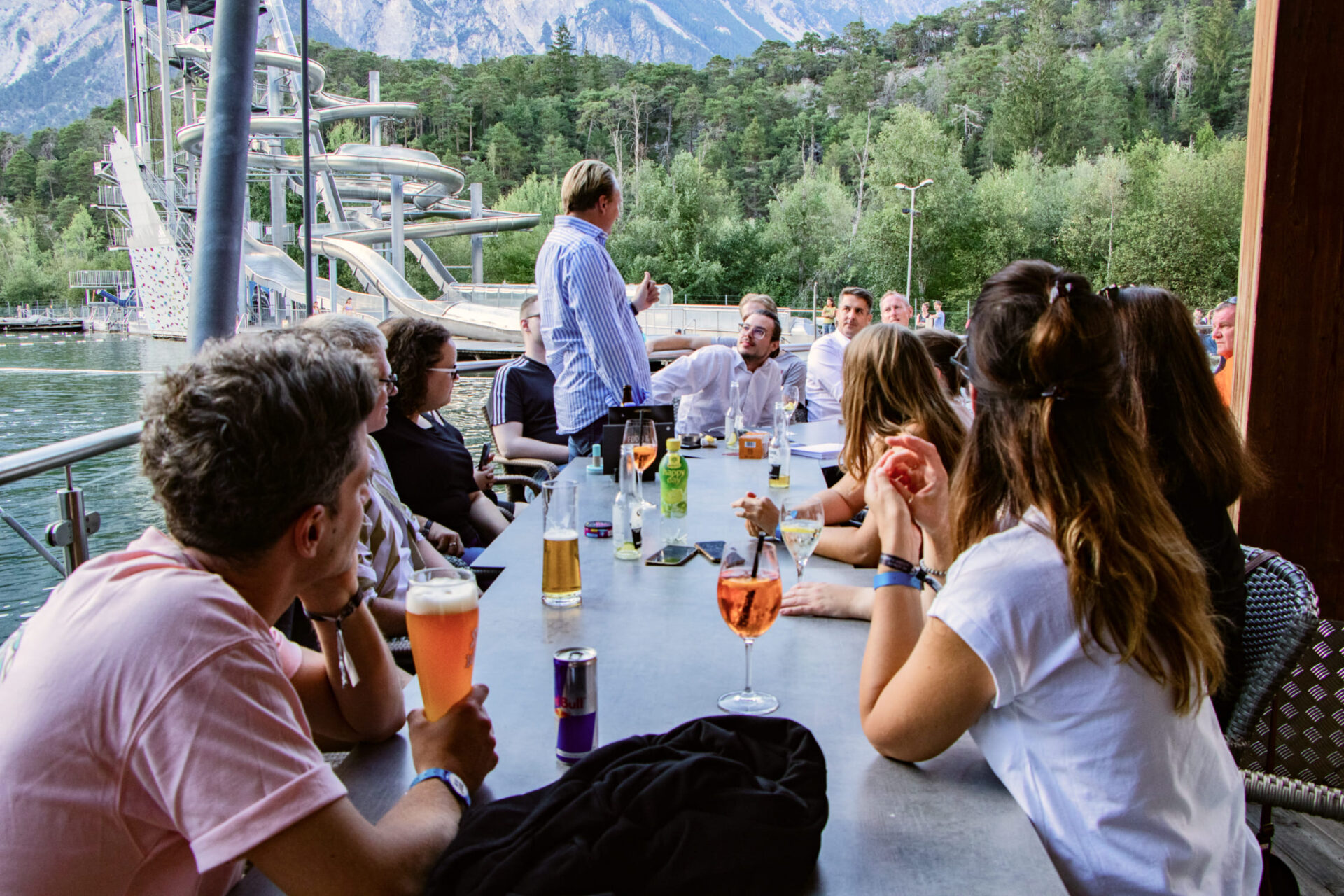 Gruppe von Personen bei einem Treffen an der Lakeside Bar in der AREA 47, Ötztal, Tirol, mit Wasserrutschen im Hintergrund