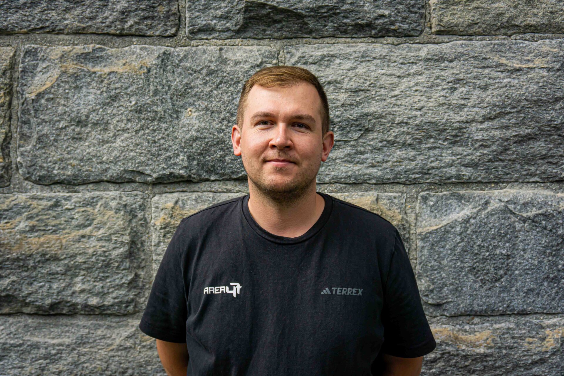Porträt eines Mitarbeiters im schwarzen AREA 47 T-Shirt vor einer Steinwand im Ötztal, Tirol