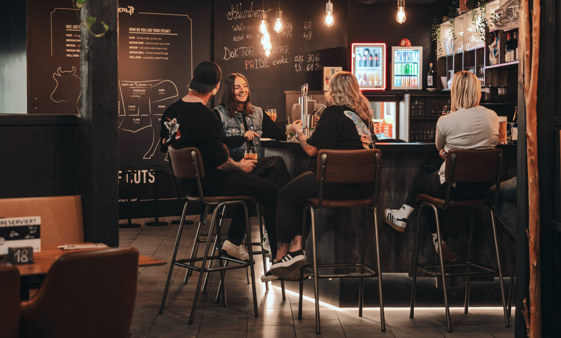 Vier Personen sitzen an der Bar im River Haus Bar & Grill der AREA 47, Ötztal, Tirol