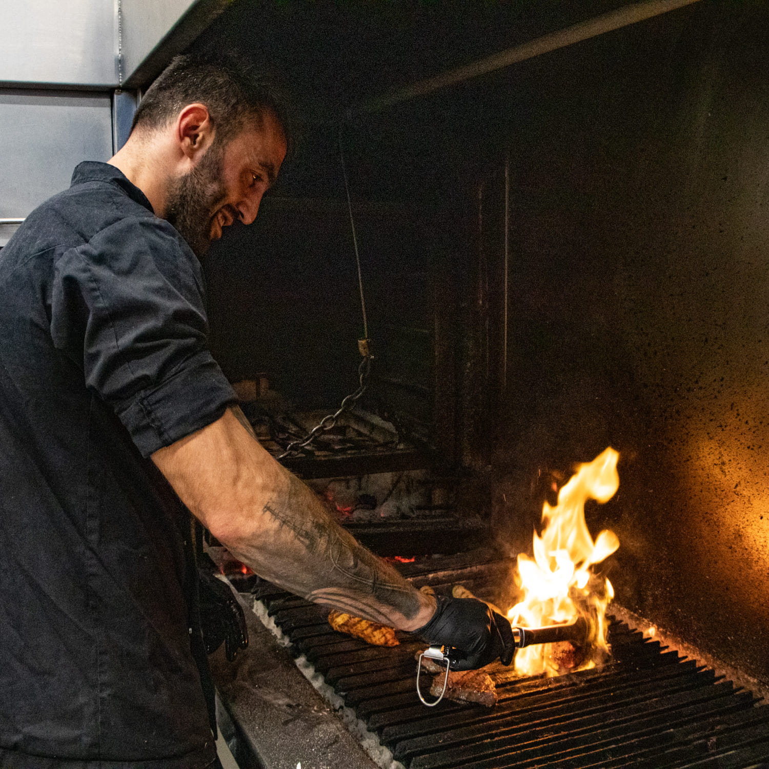 Koch grillt Fleisch auf offenem Feuer im River Haus Bar & Grill der AREA 47, Ötztal, Tirol