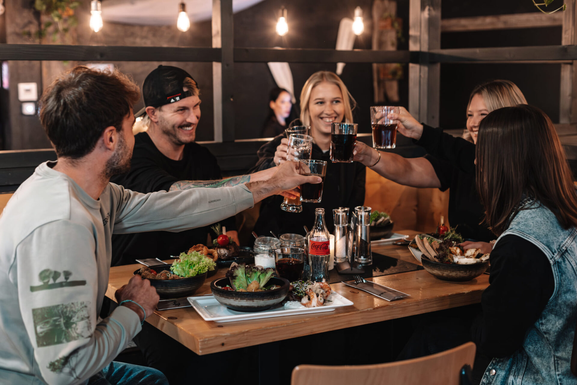 Fünf Personen stoßen beim Essen im River Haus Bar & Grill der AREA 47, Ötztal, Tirol, an