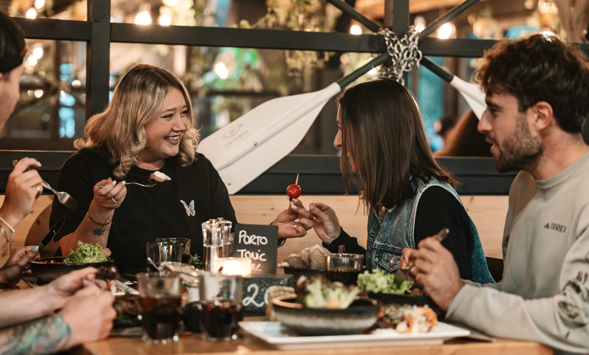 Vier Personen genießen gemeinsam ein Abendessen im River Haus Bar & Grill der AREA 47, Ötztal, Tirol