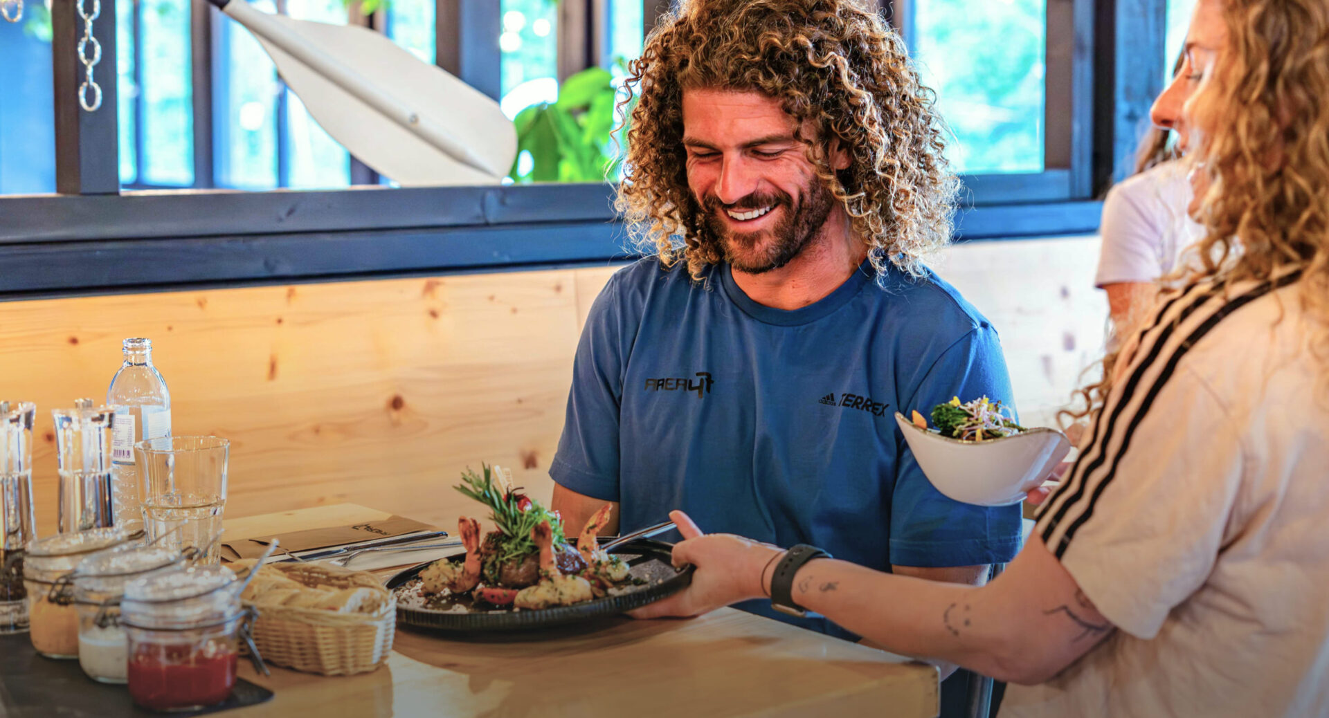 Ein Gast im River Haus Restaurant der AREA 47 im Ötztal, Tirol, wird mit einem Gericht aus Garnelen und Gemüse bedient