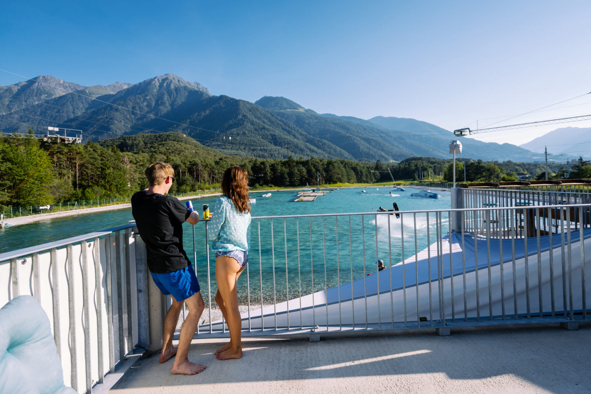 Two people enjoy the view of the Water AREA and wakeboarders at AREA 47, Ötztal, Tyrol
